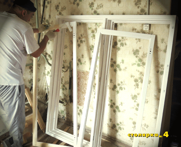 Процесс покраски деревянных окон в загородном доме. Мастер разобрал окно для удобства нанесения краски. Некоторые места проходит валиком, другие кисточкой.