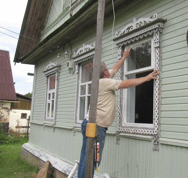 Процесс установки оконных рам в доме. Мастер высталяет окно с фрамугой.