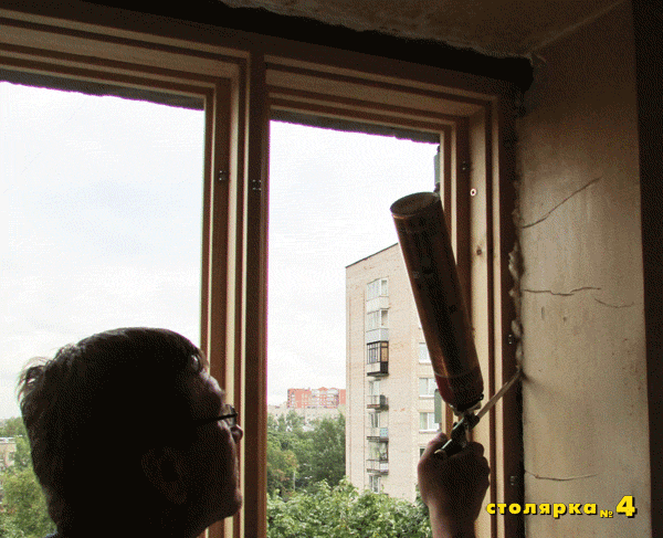 Мастер заполняет монтажной пеной шов между окном и проёмом.